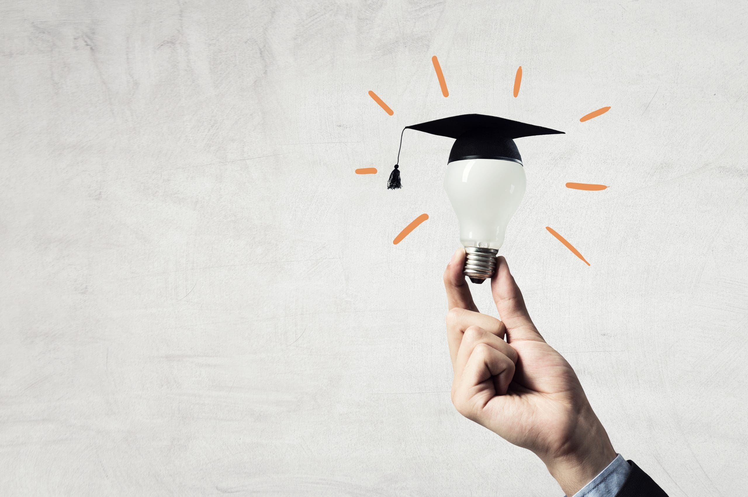 A hand holding a light bulb with a graduation cap on it.